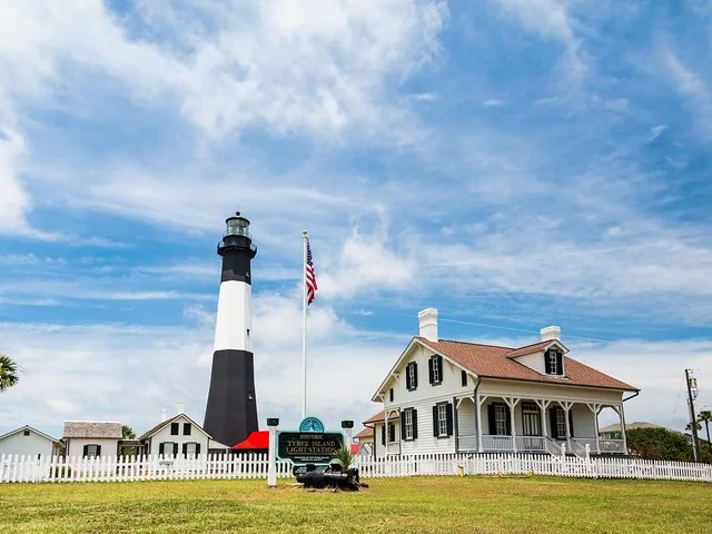 A lighthouse and white houses stand on green grass.