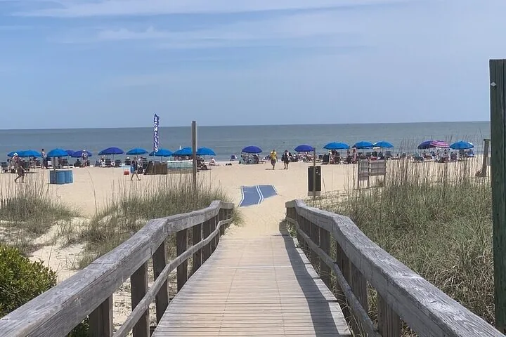 Una pasarela de madera conduce a una playa de arena con sombrillas.