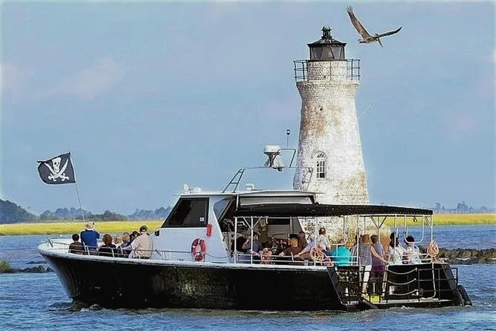 Menschen fahren mit einem Boot an einem Leuchtturm aus Backstein vorbei.